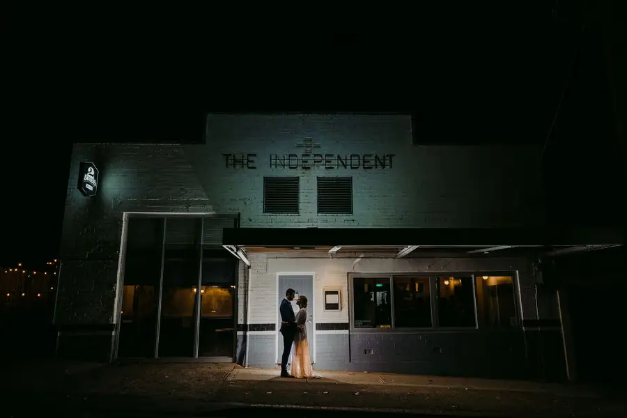 Couple stands in a brightly lit doorway of a dark reception building at night.
