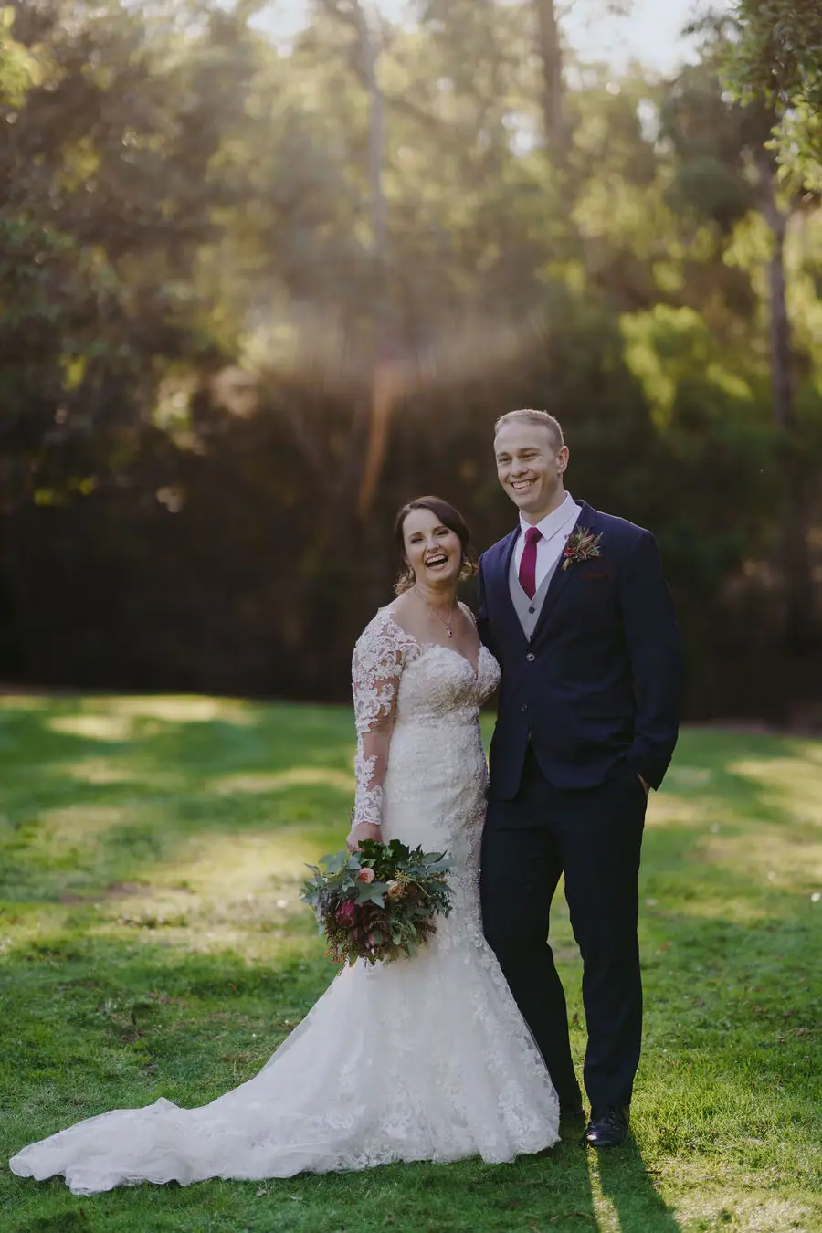 Couple poses on a garden lawn with sunlight behind them.