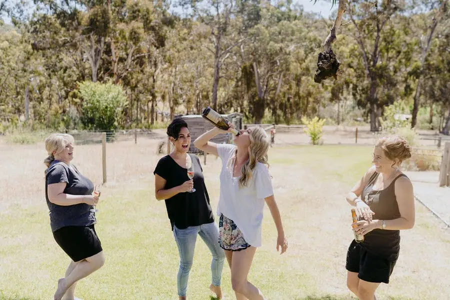 Women chat on a lawn while one drinks from a raised bottle.