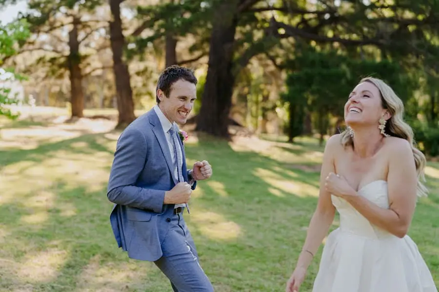 Couple laughs together beneath trees in a garden.