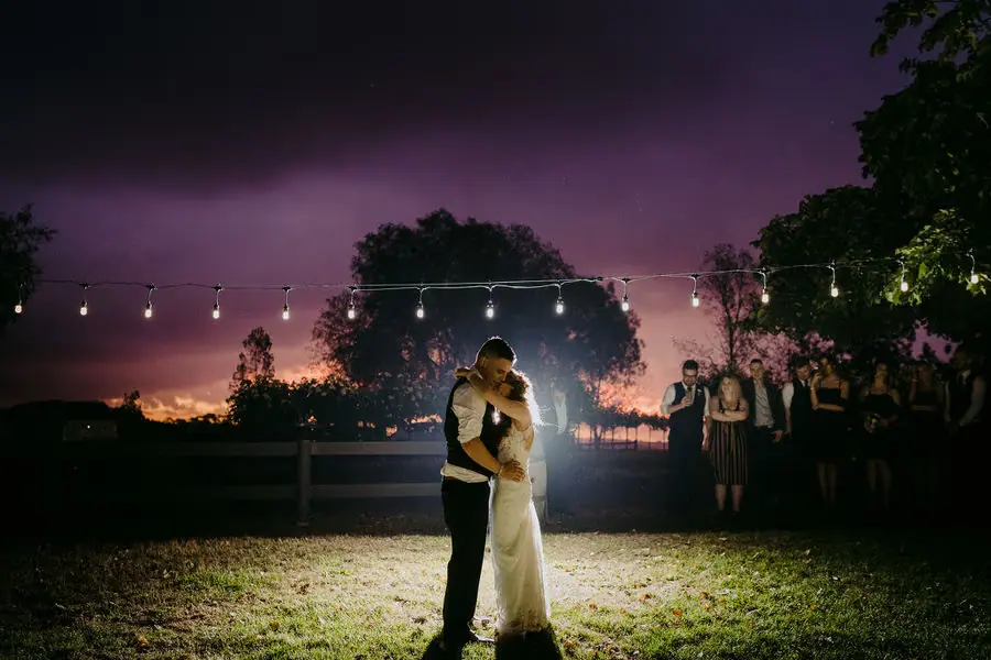 Couple embraces beneath outdoor lights against a purple evening sky.