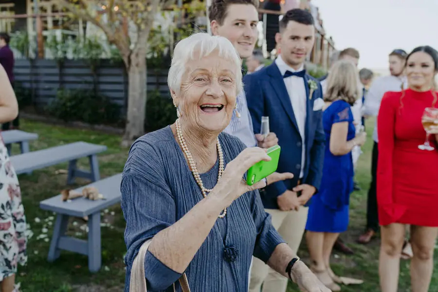 Older guest laughs while holding a bright green cup outdoors.
