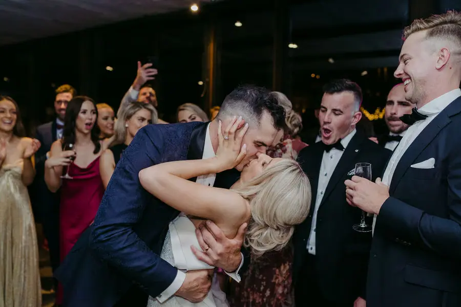 Groom dips and kisses the bride among cheering guests.