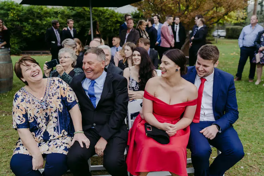 Seated guests laugh together during an outdoor ceremony.