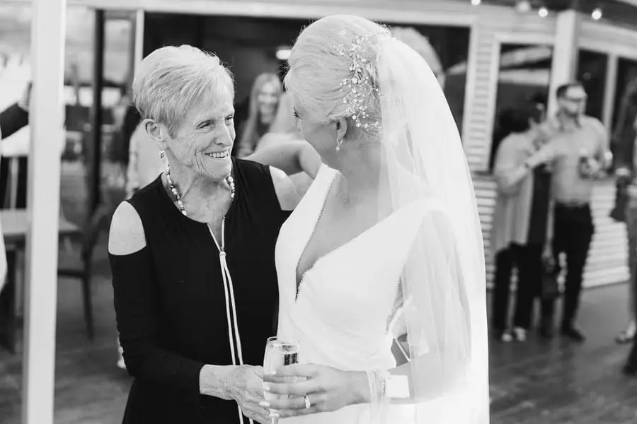 Black and white photograph of the bride greeting an older woman with a drink.