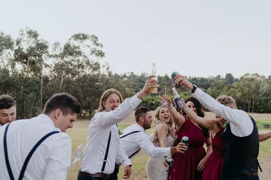 Wedding party raises drinks together outdoors.