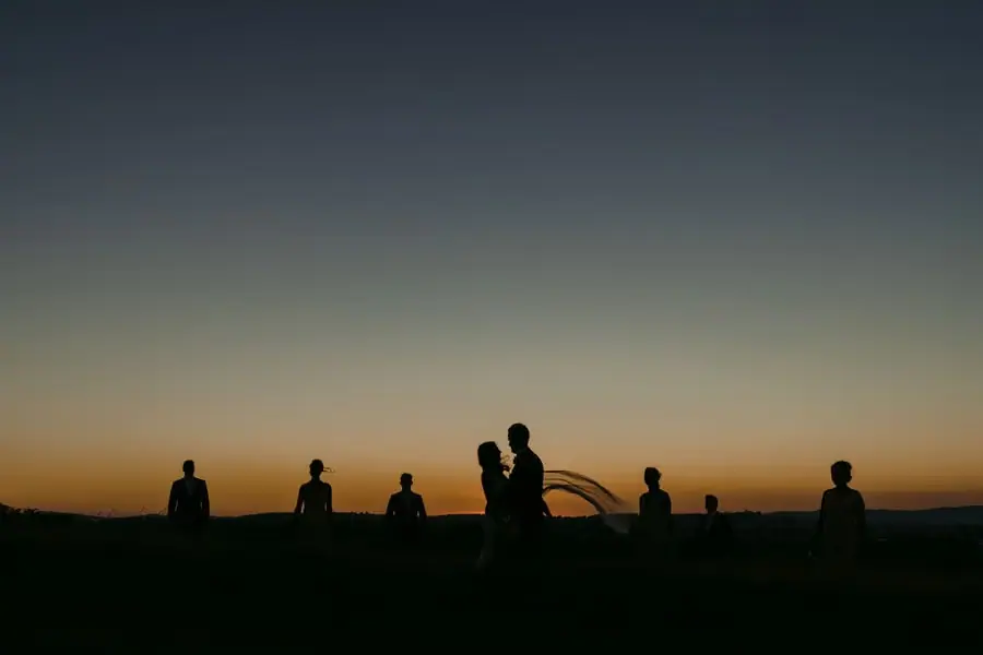 Silhouetted couple and wedding party beneath an orange sunset sky.