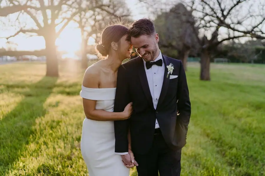 Bride leans toward the laughing groom in sunset light.