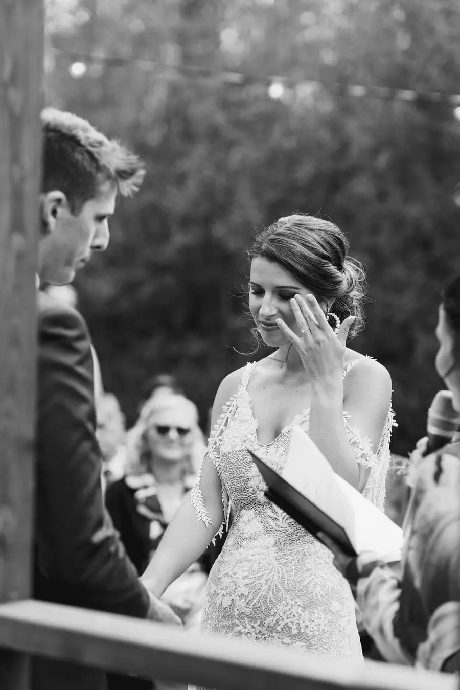 Black and white photograph of the bride wiping her eye at the ceremony.