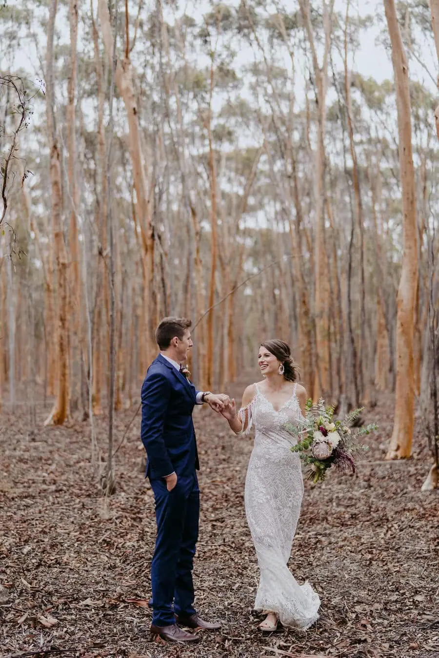 Couple faces each other among tall slender forest trees.