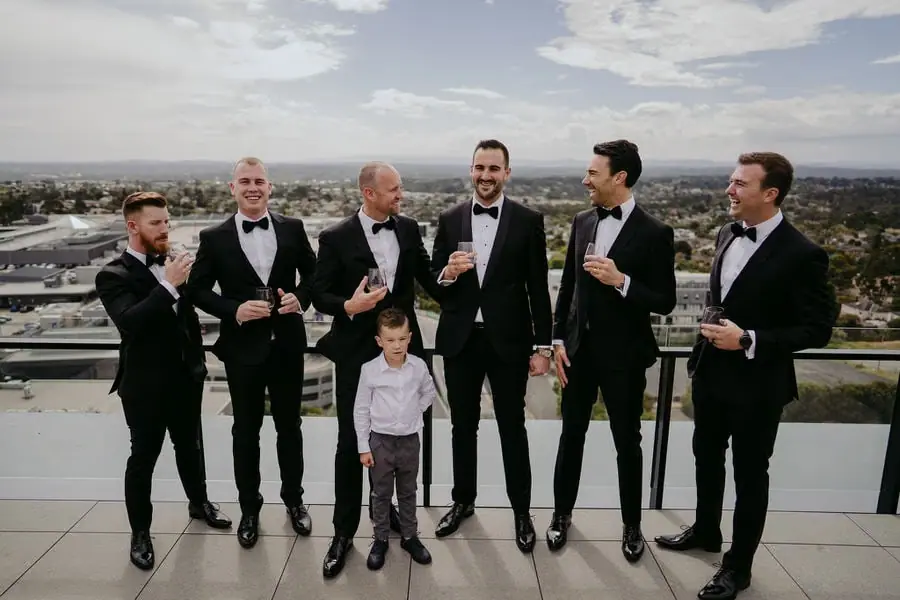 Men in suits and a young boy pose on a rooftop with city views beyond.