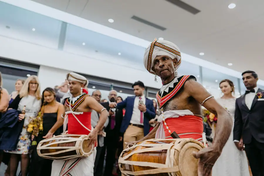 Drummers in red and gold outfits perform among reception guests.