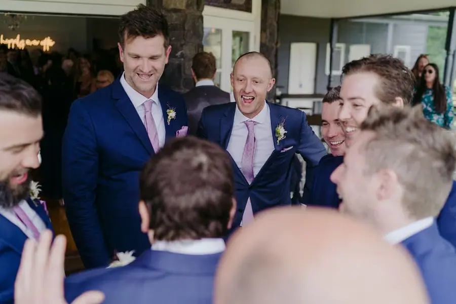 Men in blue suits laugh together among reception guests.