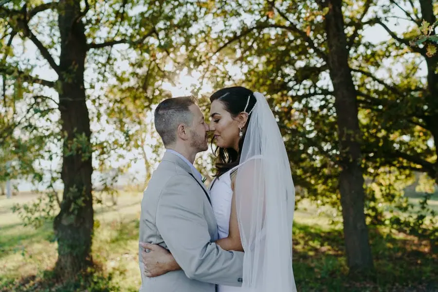 Couple kisses beneath sunlit trees.