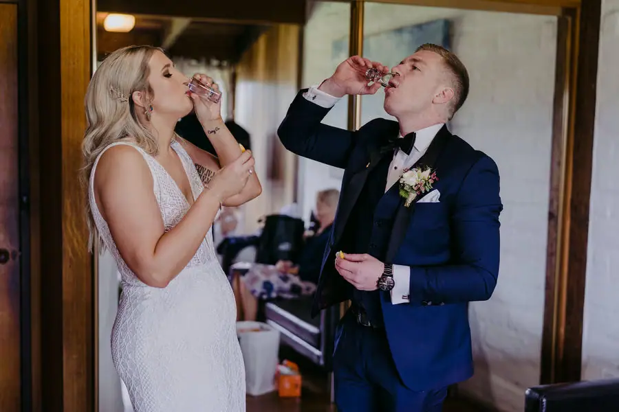 Couple drinks together from small glasses beside an open doorway.