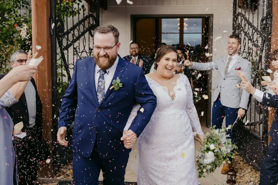 Couple exits a building through confetti tossed by guests.