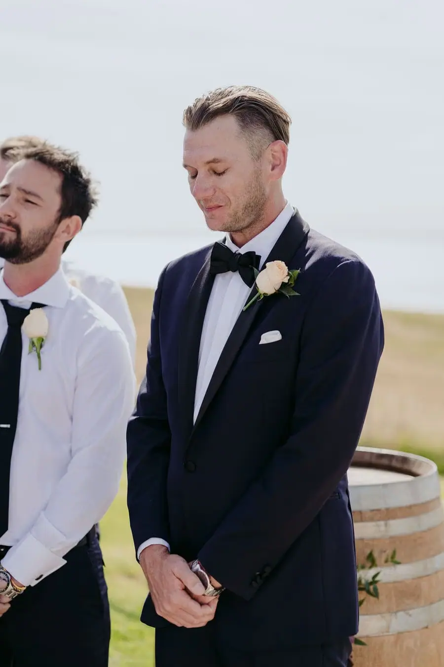 Groom stands with his hands clasped at the outdoor ceremony.