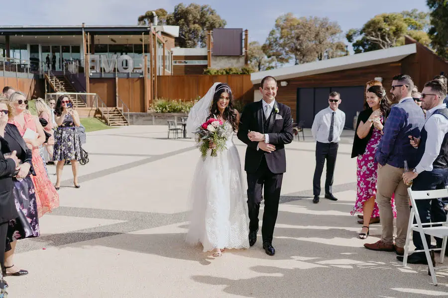Bride arrives at the outdoor ceremony with an older man beside her.