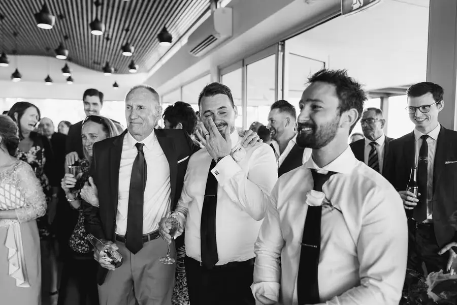 Black and white photograph of guests reacting together in a bright reception room.