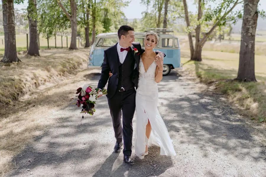 Couple walks together along a tree-lined road with a blue van behind them.