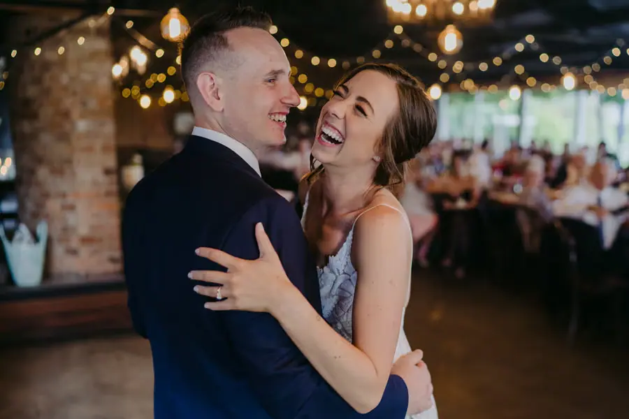 Couple laughs while embracing on the reception dance floor.