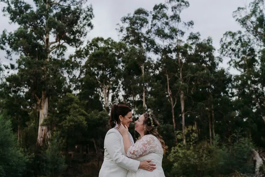 Two brides kiss in a wooded garden.