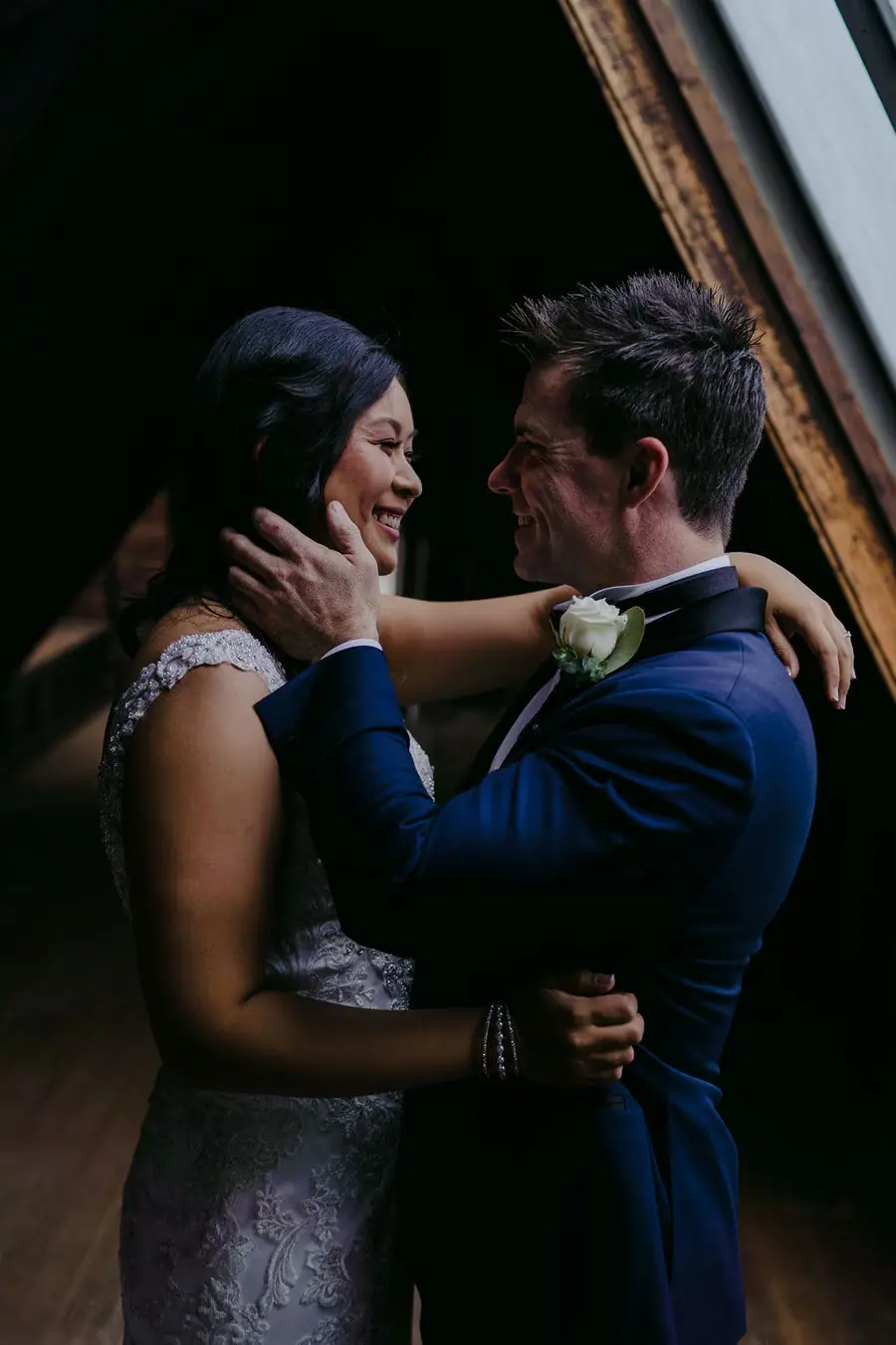 Couple embraces in a dark doorway with the groom holding the bride's face.