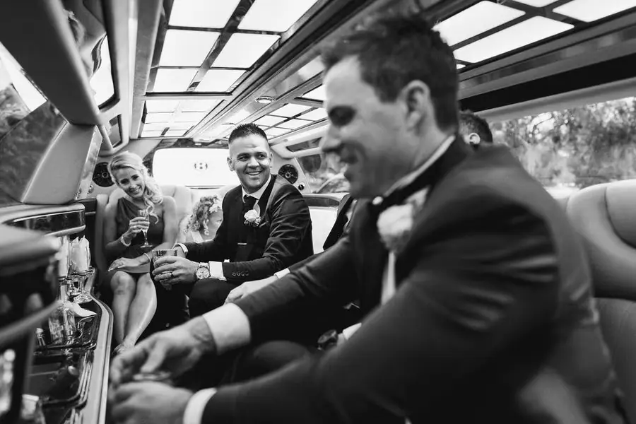 Black and white photograph of guests and the groom seated inside a vintage vehicle.