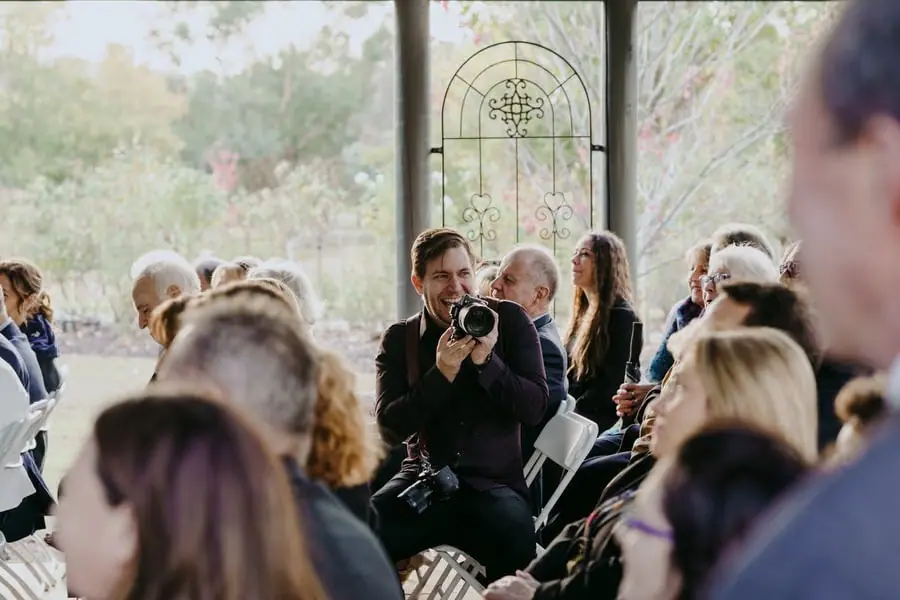 Photographer holds a camera while seated among ceremony guests.