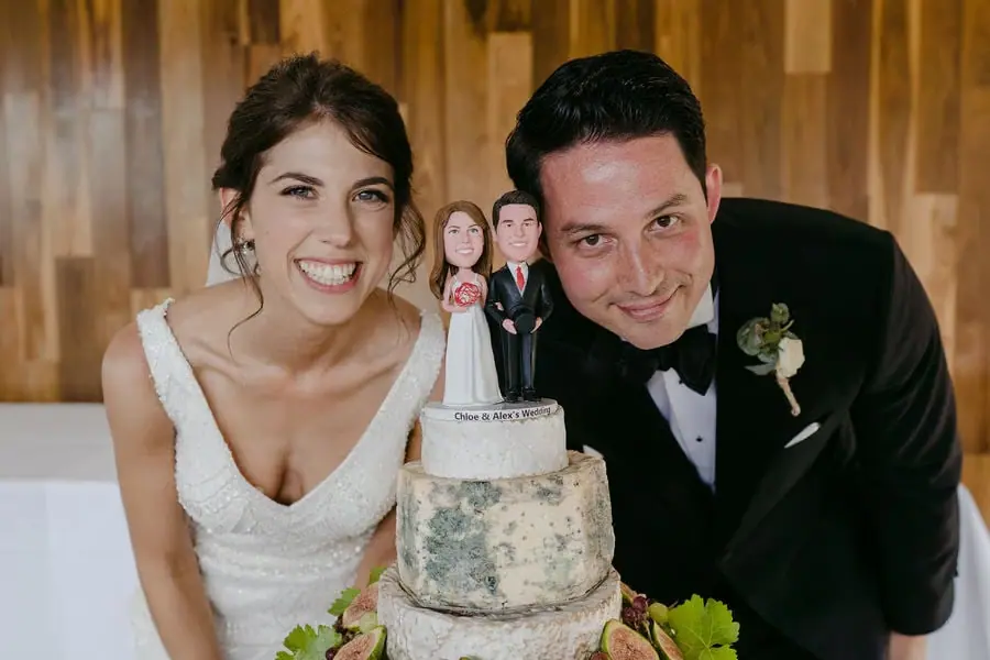 Couple smiles beside their tiered wedding cake topped with figurines.