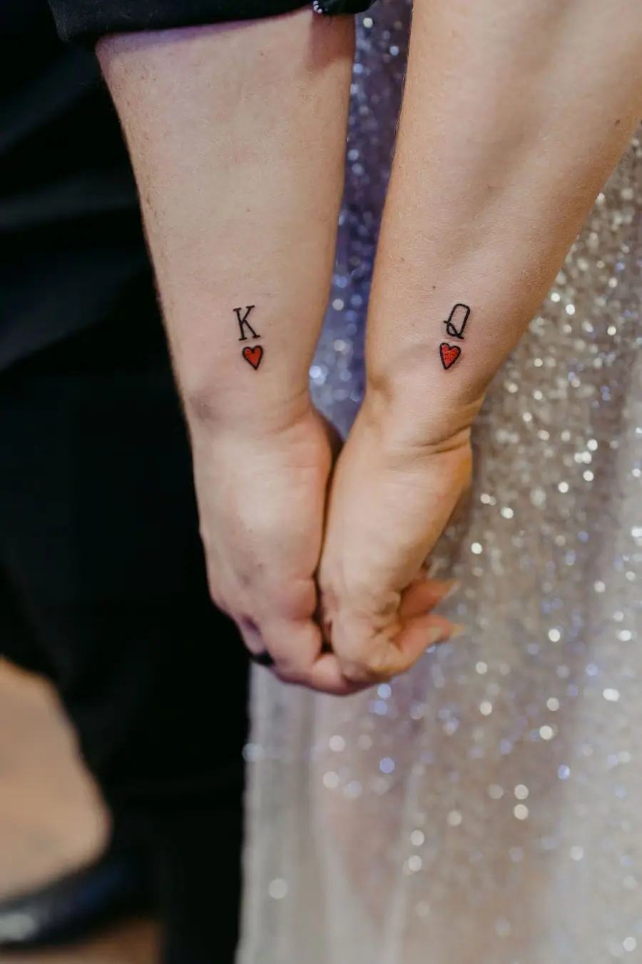 Close view of joined hands beneath king and queen of hearts wrist tattoos.