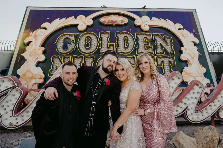 Couple and two guests pose together in front of colourful vintage signs.