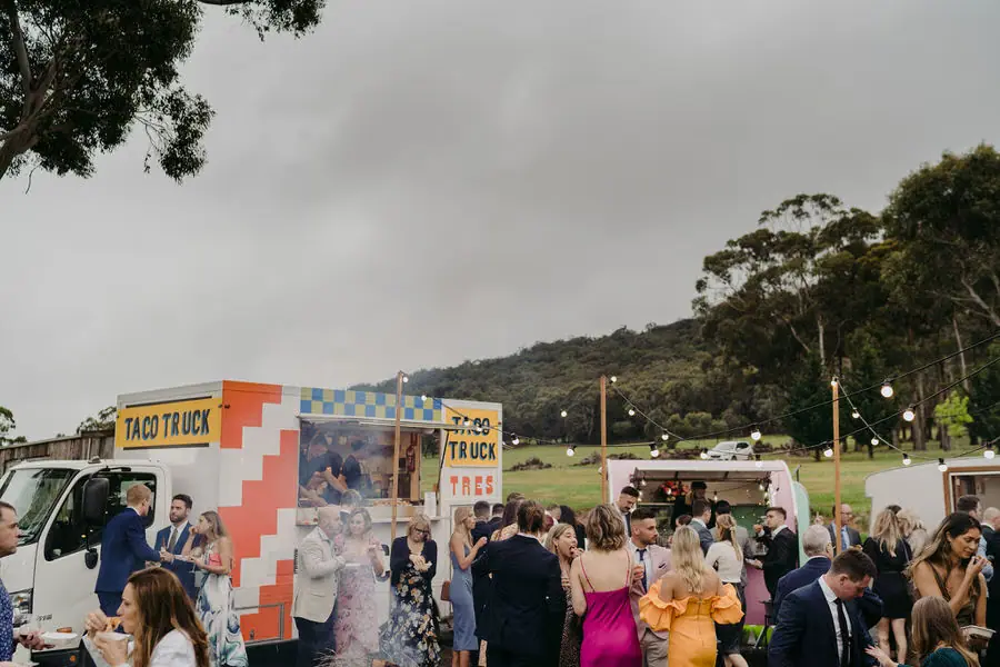 Guests gather around colourful food trucks at an outdoor reception.