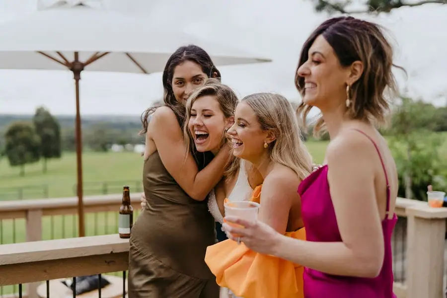 Women laugh together holding drinks on a terrace.