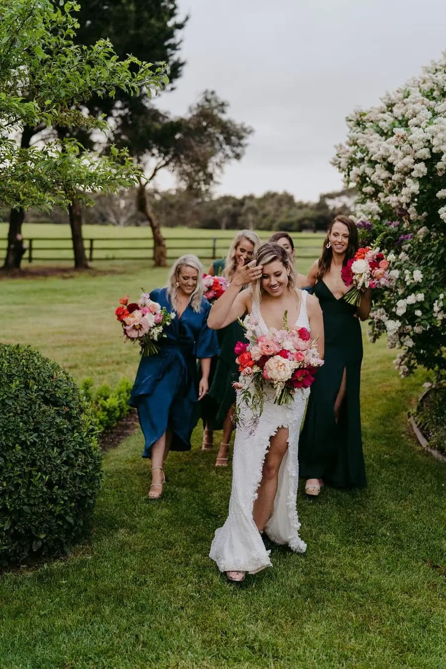Bride and bridesmaids walk toward the camera holding colourful bouquets.