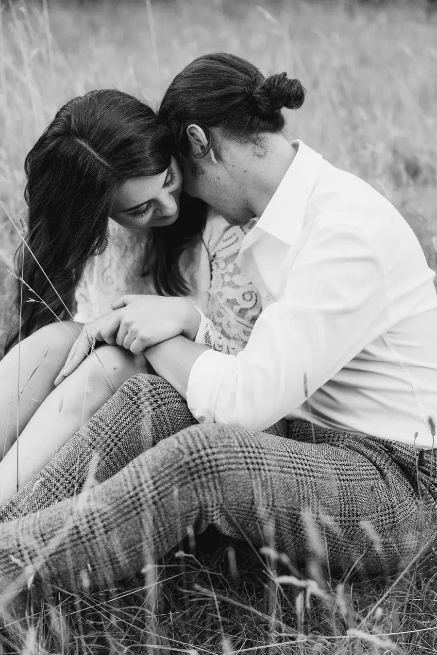 Black and white photograph of the couple sitting close together in long grass.