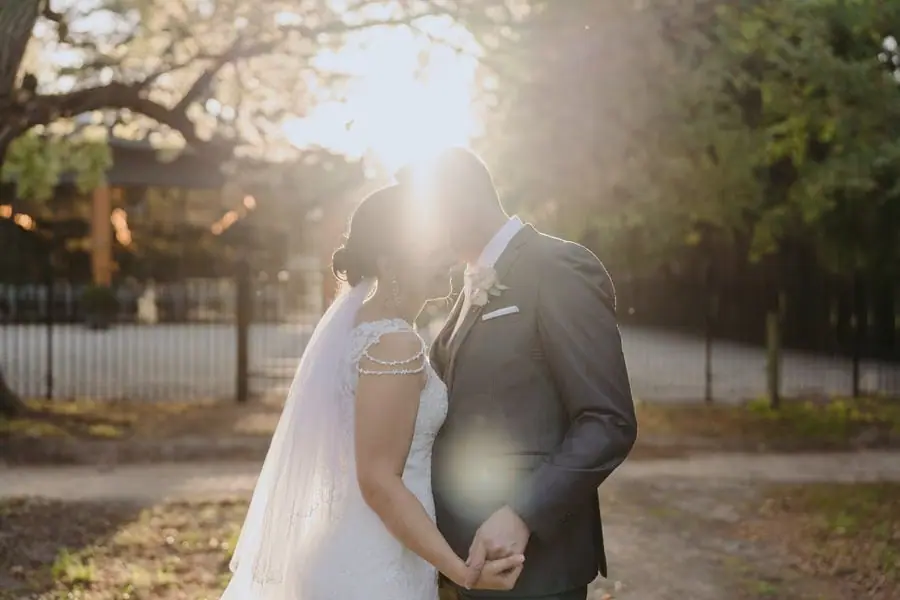 Couple holds hands and kisses with bright sunset light behind them.