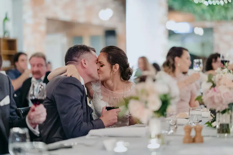 Couple kisses while seated at the reception table.