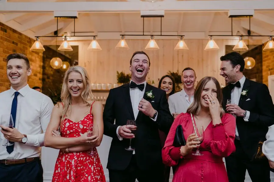 Guests laugh together holding drinks in a bright reception room.