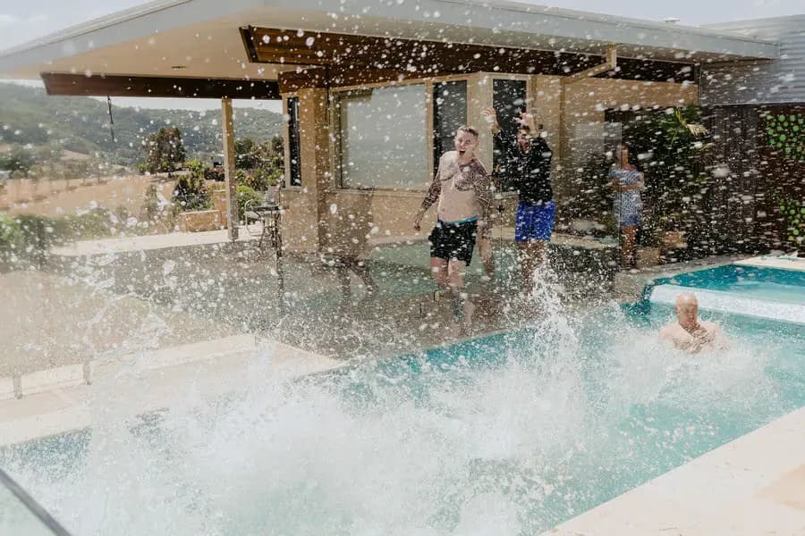 Water splashes from a swimming pool with guests standing beside it.