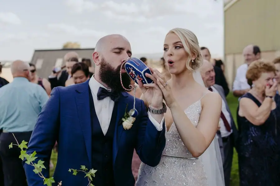 Groom drinks from a shoe beside the reacting bride and wedding guests.