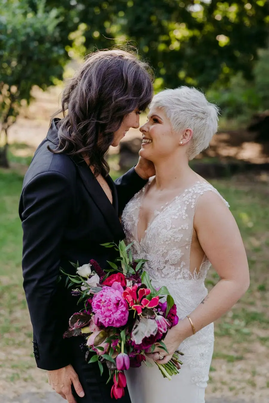 Couple kisses in a garden with the bride holding a pink bouquet.