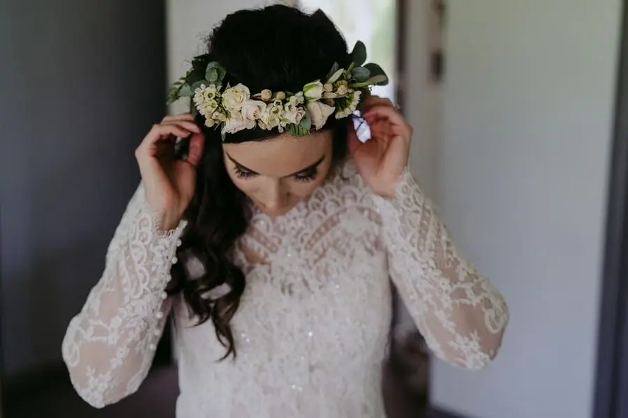 Bride adjusts a white floral crown indoors.