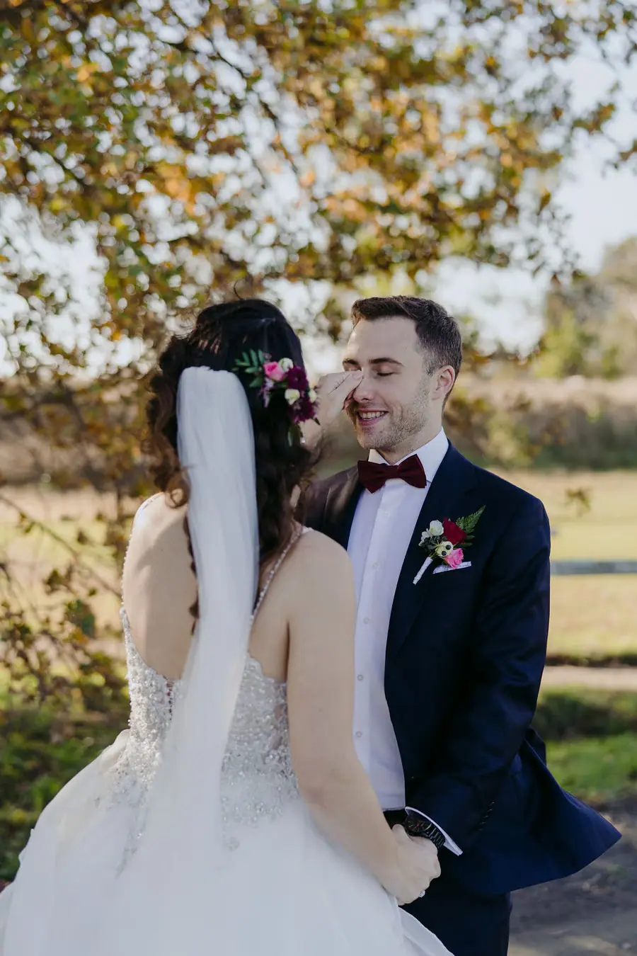 Couple kisses beneath trees with the bride's veil flowing behind her.