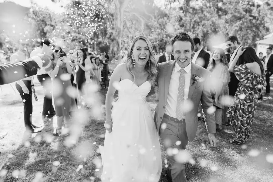 Black and white photograph of newlyweds walking through a shower of champagne spray.