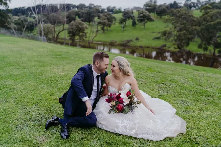 Couple sits together on a grassy slope beside a pond.