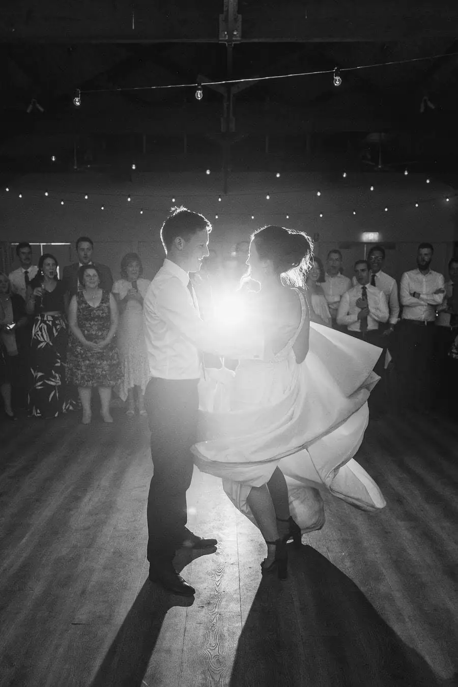 Black and white photograph of the couple dancing with bright backlighting between them.