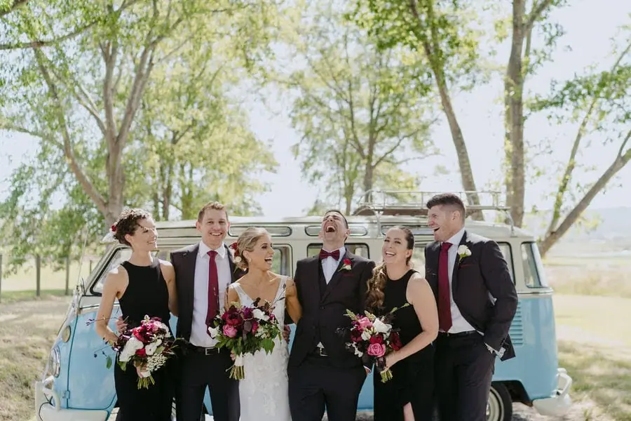 Wedding party laughs together beside a blue van.