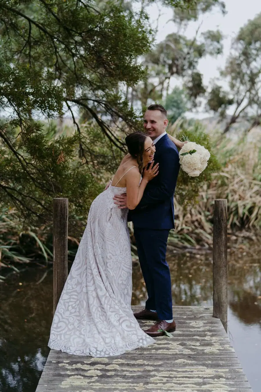 Couple embraces on a small platform beside wooded water.