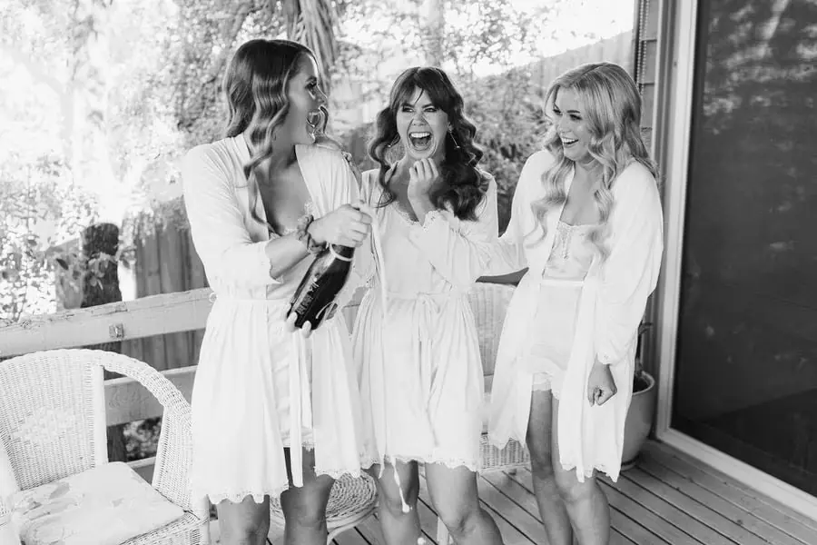 Black and white photograph of women in robes reacting to an opened bottle.